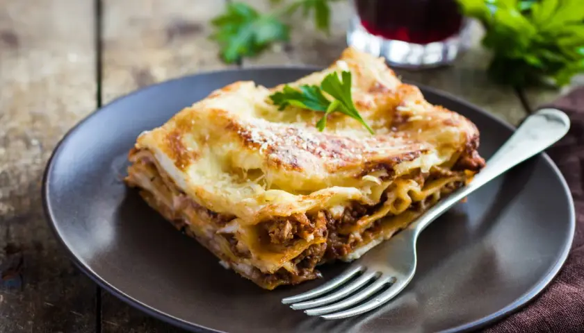 Pyszny kawałek lasagne z mięsem mielonym, idealny na prosty obiad. Posypana parmezanem i udekorowana natką pietruszki.