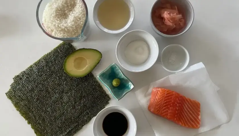 Świeży łosoś, ryż, awokado, nori i sos sojowy – oto składniki do sushi, gotowe do przygotowania pysznego posiłku.