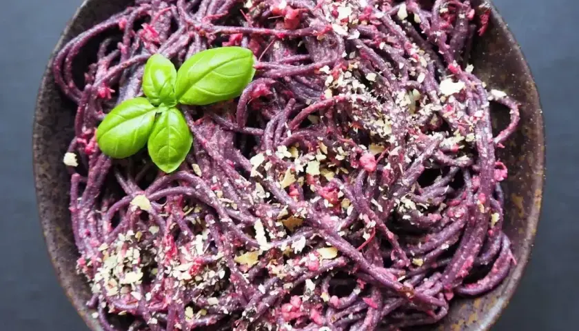 Fioletowy makaron z pesto ze słoika, posypany orzechami i udekorowany listkiem bazylii.