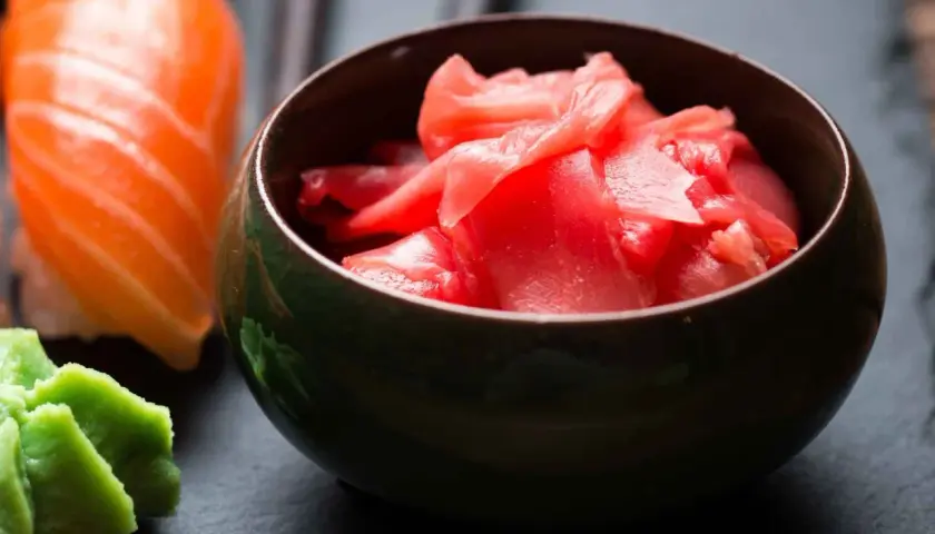 Miseczka z różowym, marynowanym imbirem obok sushi i wasabi. Idealny dodatek do japońskich smaków.