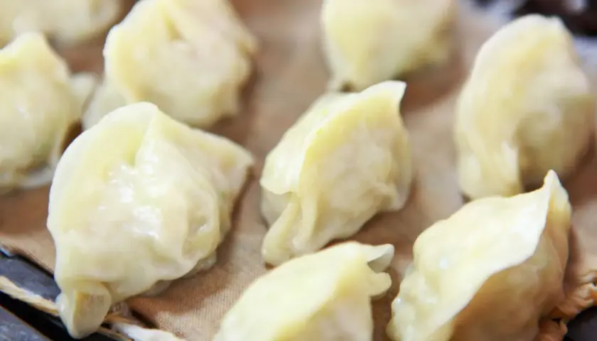 Parowane pierożki dim sum, delikatnie ułożone na brązowym papierze, kuszą swoim wyglądem.
