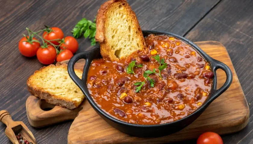 Pyszne dania na obiad: aromatyczne chili con carne z fasolą i kukurydzą, podane z chrupiącym pieczywem i świeżymi pomidorkami.