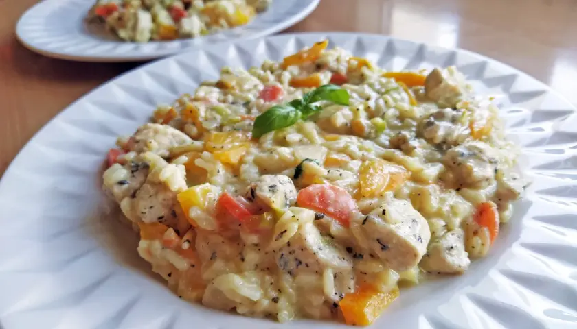 Szybkie risotto z warzywami i kurczakiem, udekorowane listkiem bazylii. Pyszne i kolorowe danie na talerzu.