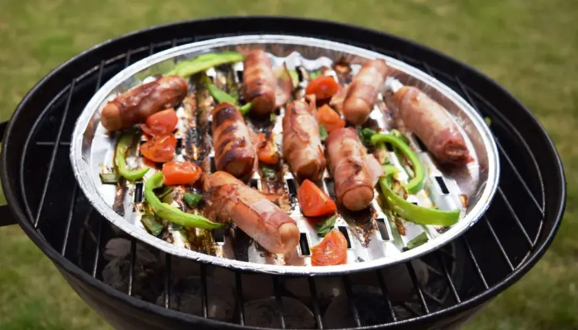 Pyszna kiełbasa z grilla, zawinięta w boczek, pieczona z papryką i pomidorkami na rozgrzanym ruszcie.