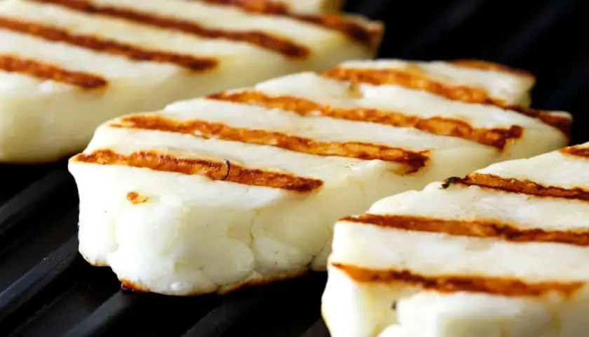 Trzy kawałki halloumi z grilla, z apetycznymi paskami, leżą na czarnej, grillowej powierzchni.