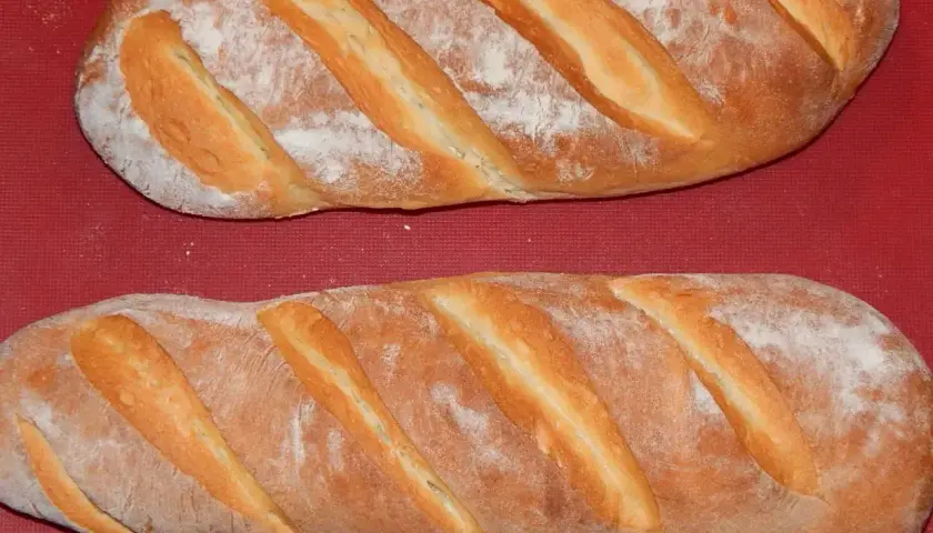 Dwie świeże bułki wrocławskie, lekko oprószone mąką, leżą na czerwonym tle.
