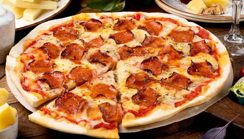Pyszna pizza pepperoni z ciągnącym serem, obok serowe dodatki do pizzy, winogrona i kieliszek czerwonego wina.