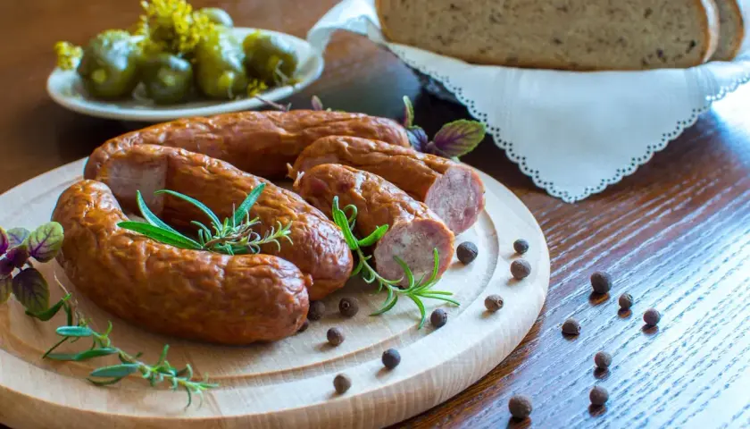 Pyszna kiełbasa z piekarnika, podana z chlebem i ogórkami, ozdobiona rozmarynem i pieprzem.