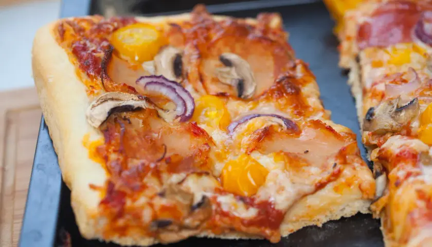 Domowa pizza na blachę, pachnąca świeżymi drożdżami, z pieczarkami, cebulą i pomidorkami. Idealna na rodzinny obiad.