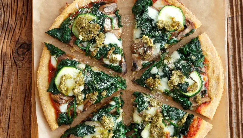 Pyszna pizza ze szpinakiem, cukinią i grzybami, polana sosem pesto.