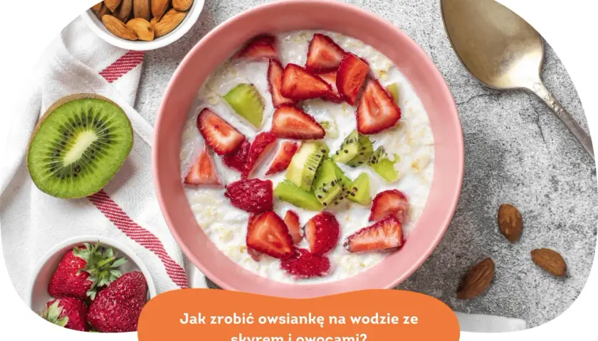 Pyszna owsianka z owocami: truskawkami i kiwi, podana w różowej miseczce. Obok migdały i łyżka.
