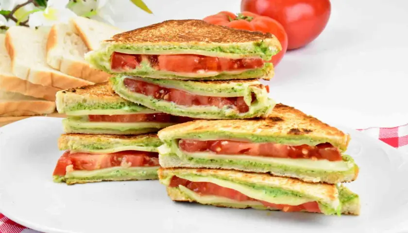 Pyszne włoskie kanapki z serem, pomidorami i zielonym pesto, ułożone na talerzu.