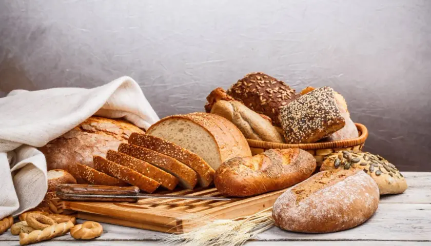 Różnorodne pieczywo, od bochenków po bułki, ułożone na desce. Idealne do odświeżenia bułki na śniadanie.