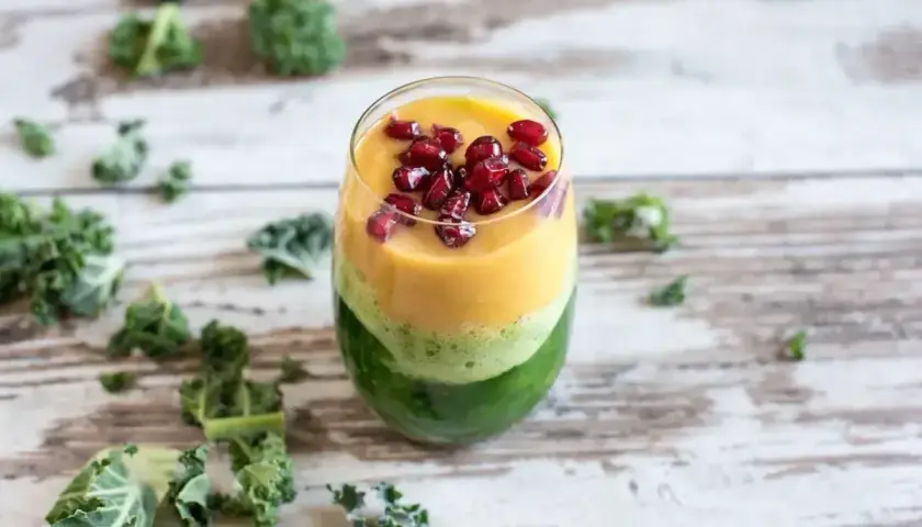 Warstwowy koktajl z jarmużu, mango i granatu, ozdobiony pestkami granatu.