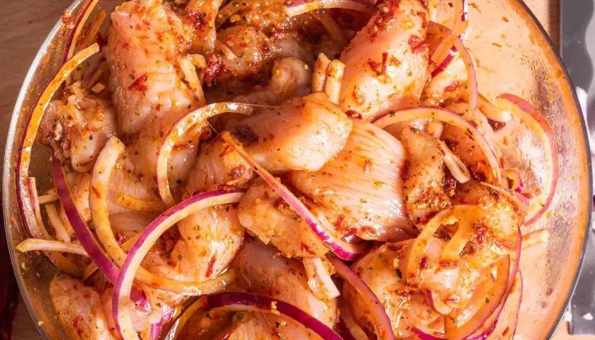 Kawałki kurczaka w misce, gotowe do grillowania. Marynata do kurczaka na grilla z cebulą i przyprawami.