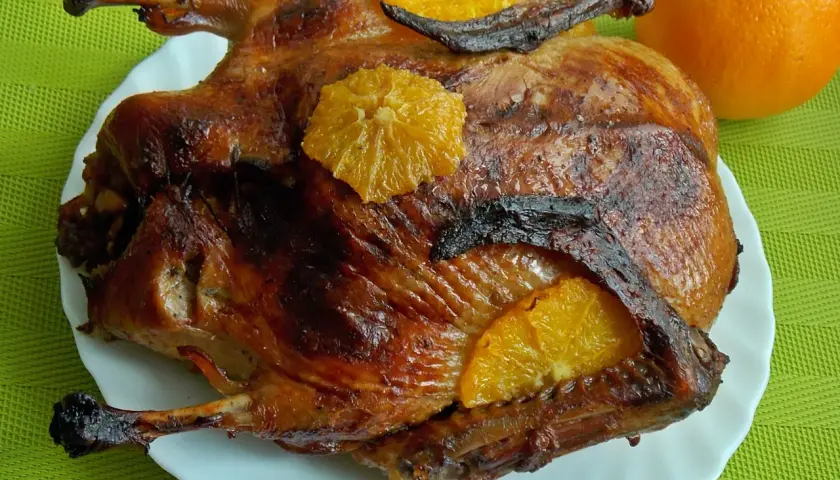 Pieczona kaczka w pomarańczach, złocista i apetyczna, ozdobiona plasterkami cytrusów.