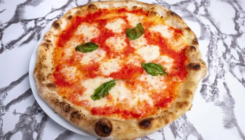 Pyszne ciasto na pizzę neapolitańską z pomidorami, mozzarellą i bazylią, idealne na letni wieczór.