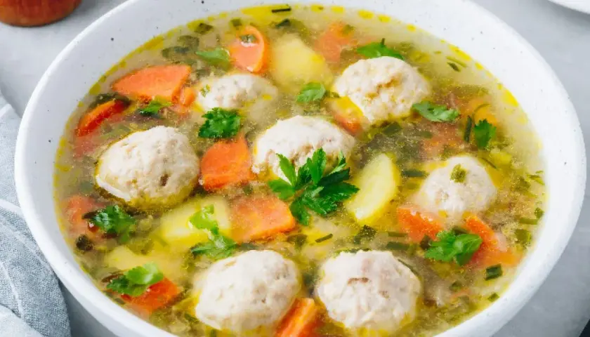 Zupa klopsowa babci: aromatyczny bulion z klopsikami, ziemniakami i marchewką, posypana natką pietruszki.
