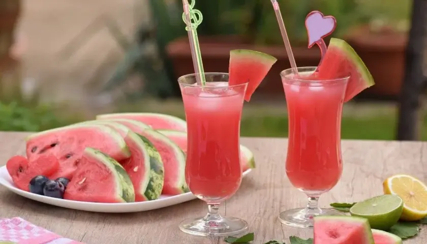 Orzeźwiająca lemoniada arbuzowa z plasterkami arbuza, cytryny i limonki na drewnianym stole.