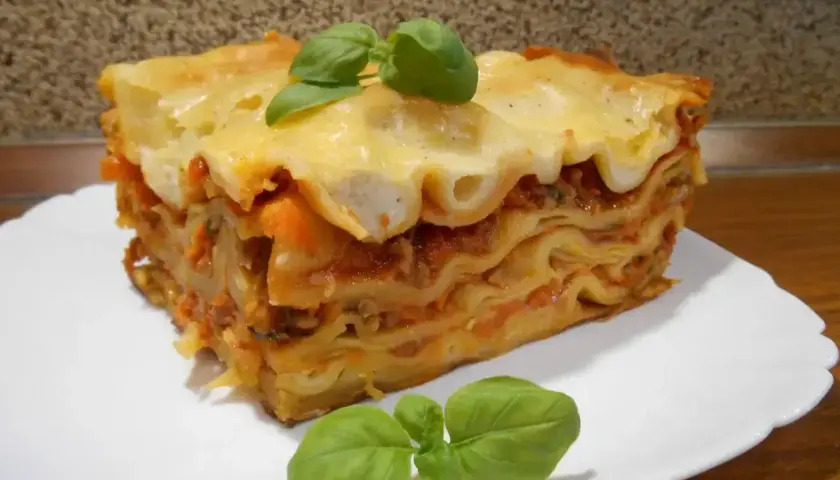 Pyszna, wielowarstwowa lasagne z sosem pomidorowym i serem, ozdobiona listkami bazylii. Idealna inspiracja, jak zrobić lasagne.