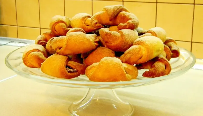 Stos rogalików drożdżowych, przygotowanych według przepisu babci, na szklanej paterze.