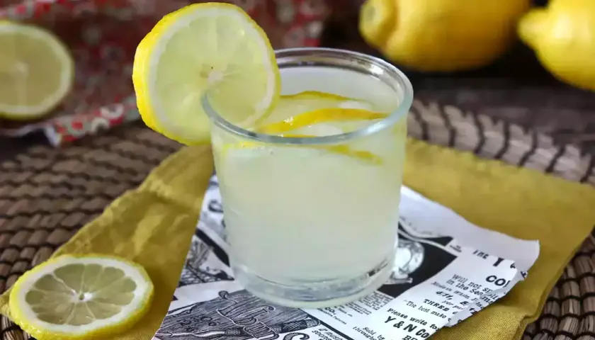Orzeźwiający drink z limoncello, ozdobiony plasterkiem cytryny, na tle cytryn i wzorzystej tkaniny.