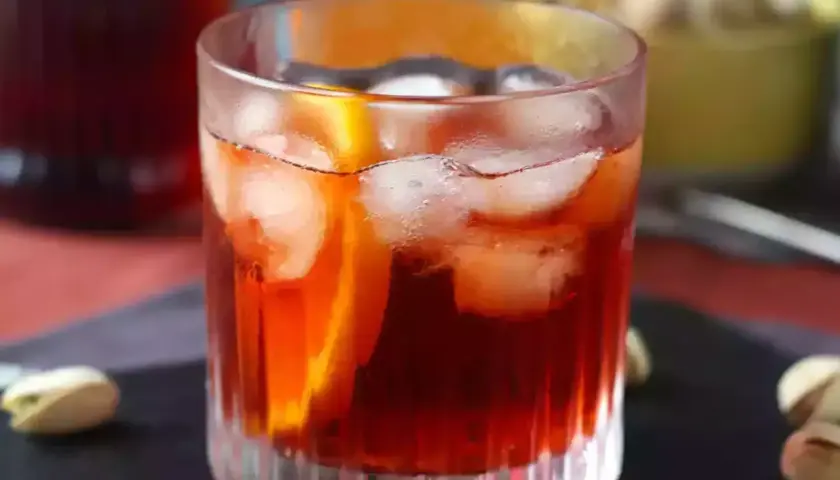 Klasyczny negroni przepis: czerwony koktajl z lodem i pomarańczą w szklance, obok pistacje.