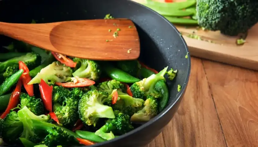 Brokuły, groszek cukrowy i papryczka chili w woku, gotowe do stir fry. Drewniana łopatka miesza warzywa.