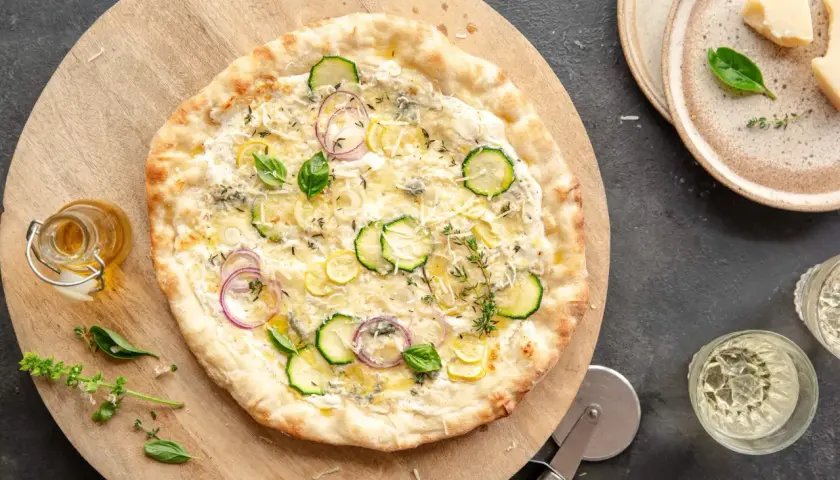 Pyszna pizza bianca z cukinią, cebulą i cytryną, podana na drewnianej desce.