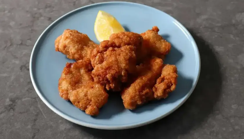 Chrupiące kawałki kurczaka karaage na niebieskim talerzu, ozdobione ćwiartką cytryny. Idealna przekąska.