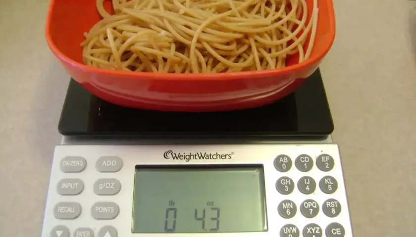 Porcja makaronu w czerwonej misce na wadze cyfrowej. Waga pokazuje 0.43 funta, co pomaga w ustaleniu, jak liczyć kalorie makaronu.