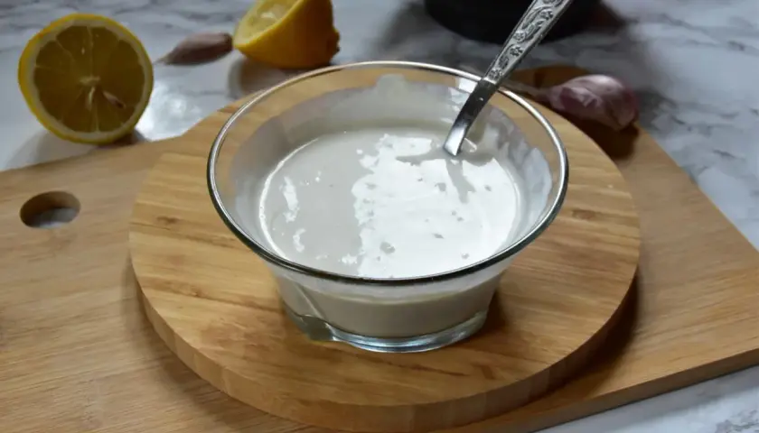 Kremowe aioli w miseczce, obok cytryna i czosnek. Idealne do dipów i sosów.