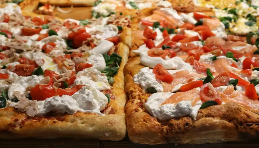Dwie prostokątne pizze z burratą, pomidorkami i łososiem lub tuńczykiem. Puszyste ciasto, kremowy ser i świeże dodatki kuszą swoim wyglądem.