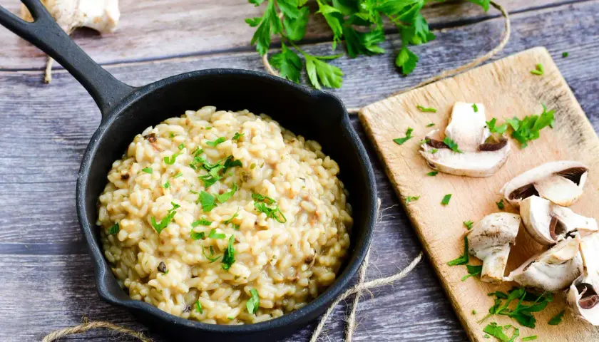 Kremowe risotto z grzybami i natką pietruszki w czarnej patelni.