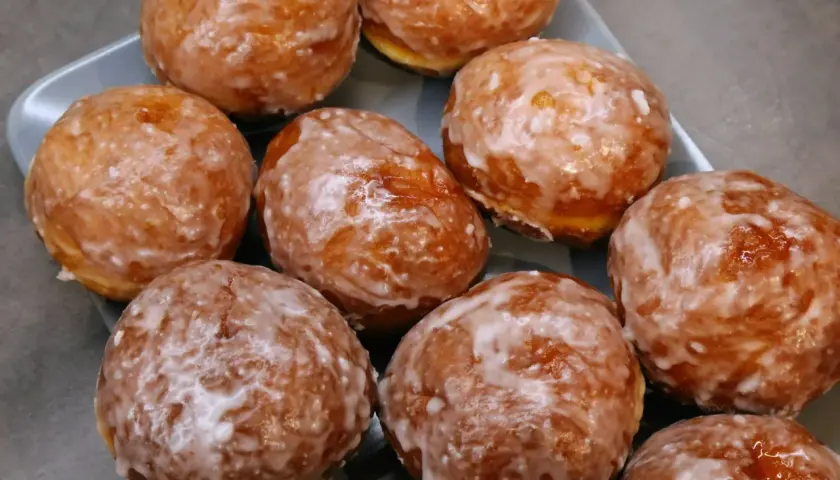 Pyszne, rumiane, pieczone paczki z lukrem, ułożone na szarej tacy. Idealne na tłusty czwartek.