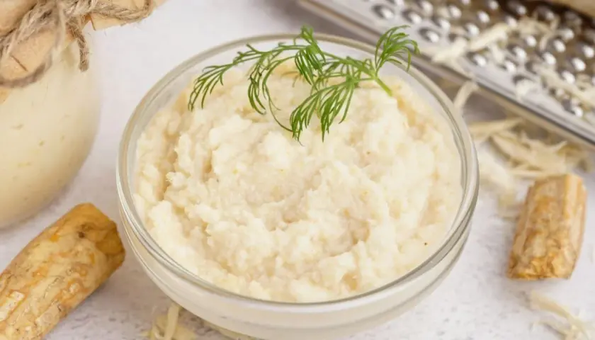 Domowy chrzan do słoików: świeży korzeń, tarta masa w misce i słoik z przetworem.