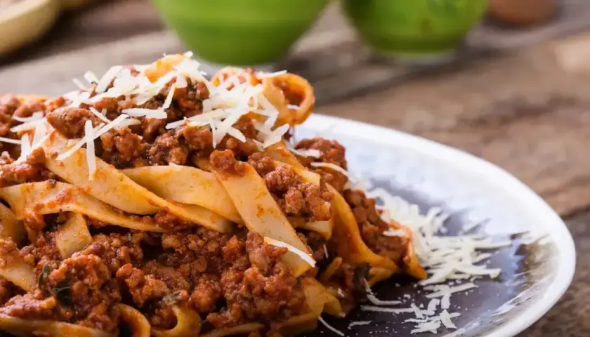 Pyszne tagliatelle z sosem bolognese, posypane parmezanem. Idealne danie, gdy zastanawiasz się, ile smażyć mięso mielone do spaghetti.