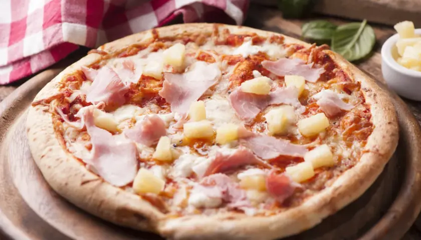Apetyczna pizza z ananasem i szynką, polana ciągnącym się serem, na drewnianej desce.