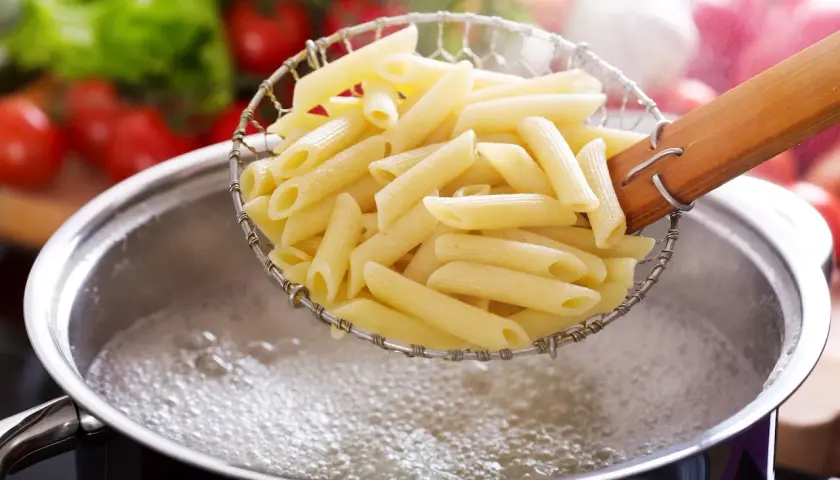 Penne w cedzaku, gotowe do podania, idealnie ugotowane makaron al dente. W tle pomidory i sałata.