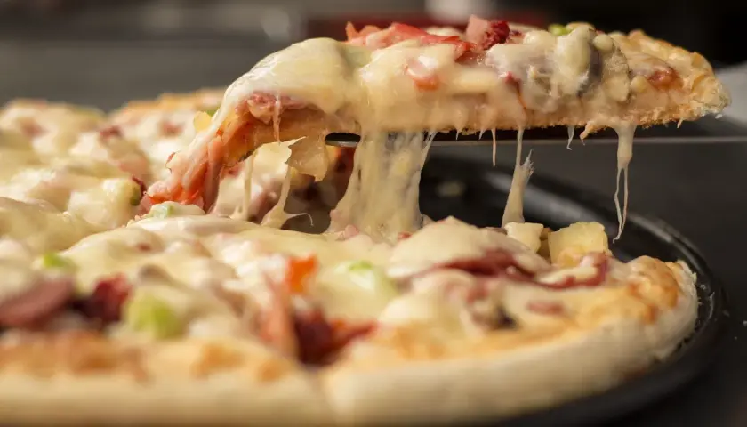Gorąca, ciągnąca się pizza mrożona z serem, szynką i ananasem. Kawałek pizzy jest podnoszony, odsłaniając roztopiony ser.