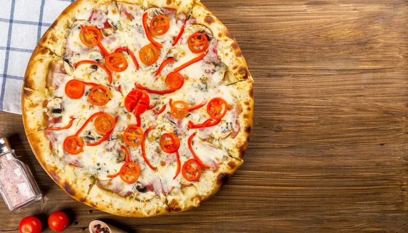 Apetyczna pizza capricciosa z pomidorkami, papryką i serem na drewnianym blacie.