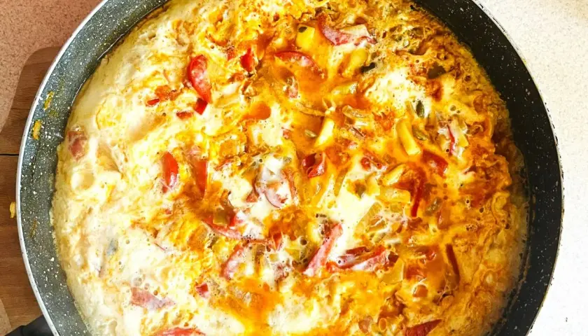 Pyszny omlet z warzywami w trakcie smażenia na patelni. Widoczne kawałki papryki i cebuli.