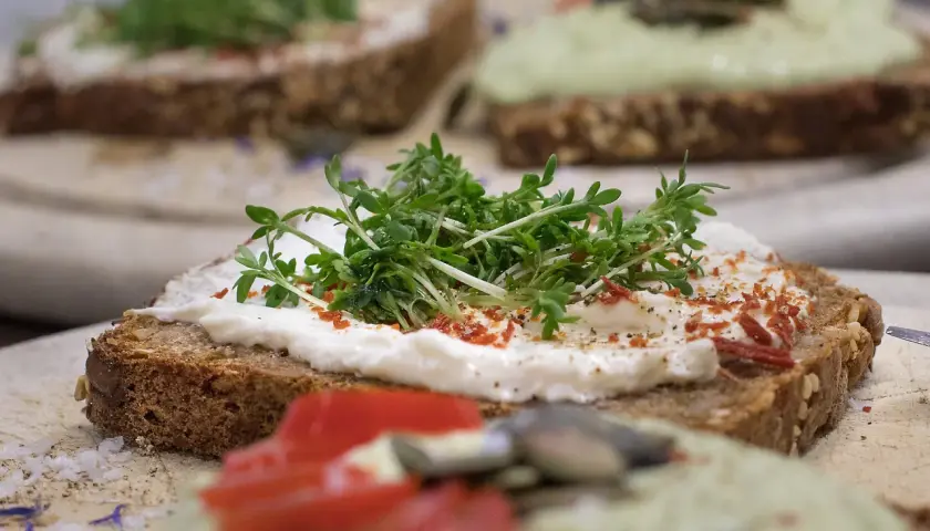 Pyszne, zdrowe pinchos na ciemnym pieczywie z serkiem, rukolą i pomidorem. Idealne na lekki posiłek.