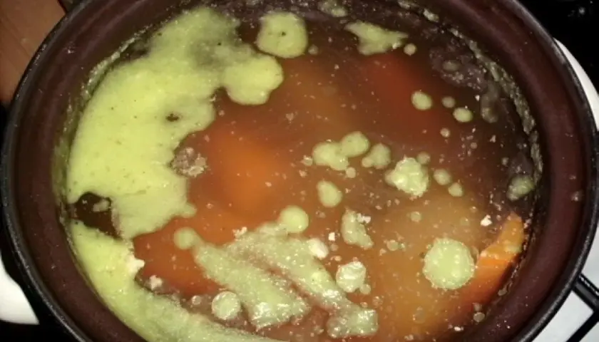 Gęsta, zielona piana na powierzchni aromatycznej zupy na rosole. Widać kawałki warzyw i mięsa.