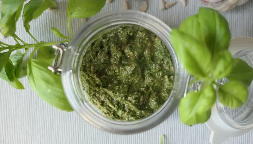 Domowe pesto z bazylii w słoiku, obok nasion słonecznika i czosnku. Idealne, by dowiedzieć się, jak zrobić pesto.
