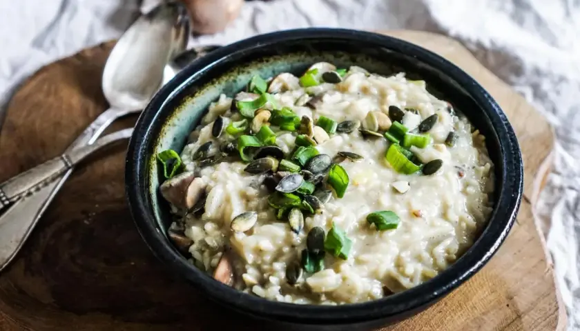 Aksamitne risotto z pieczarkami, posypane pestkami dyni i szczypiorkiem, czeka na talerzu.