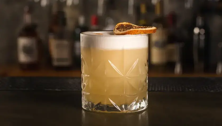 Klasyczny whisky sour przepis: orzeźwiający koktajl z pianką i plasterkiem suszonej pomarańczy.