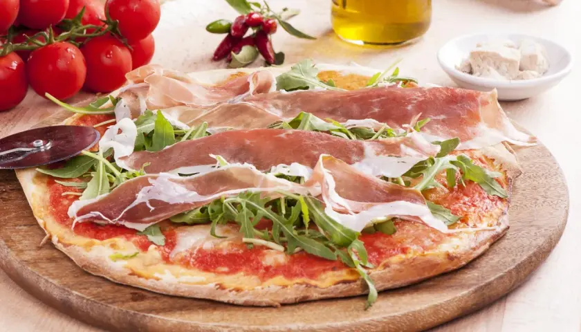 Pyszna pizza prosciutto z rukolą, pomidorami i oliwą z oliwek. Idealna na włoską ucztę.