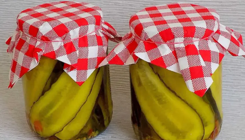 Słoiki z ogórkami w curry ze skórką, ozdobione czerwono-białymi kratkowanymi chusteczkami.