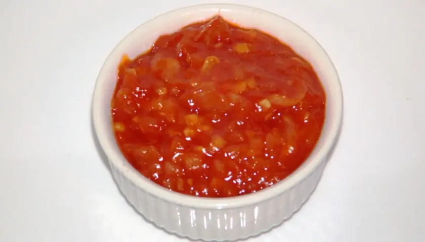 Pomarańczowy, pikantny sos piri piri w białej miseczce, gotowy do podania.
